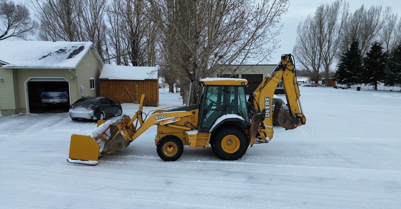 Deere 410G with snow pusher clearing a residential drive